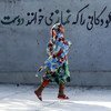 Una niña con su hiyab en Irán pasa corriendo por delante de un mural que dice, en persa, "Dios ama a los niños que rezan su "namaz" [oraciones]." (Archivo)