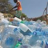 رجل كيني يرتدي قميصاً برتقالياً وتنورة خضراء يلتقط زجاجات بلاستيكية من شاطئ في واتامو، كينيا، كجزء من جهد محلي للحفاظ على المحيطات.