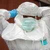 Uma profissional de saúde em Gomas, na República Democrática do Congo, ajusta um traje de proteção branco e uma touca enquanto usa luvas azuis e máscara facial em um necrotério durante o surto de Ebola.