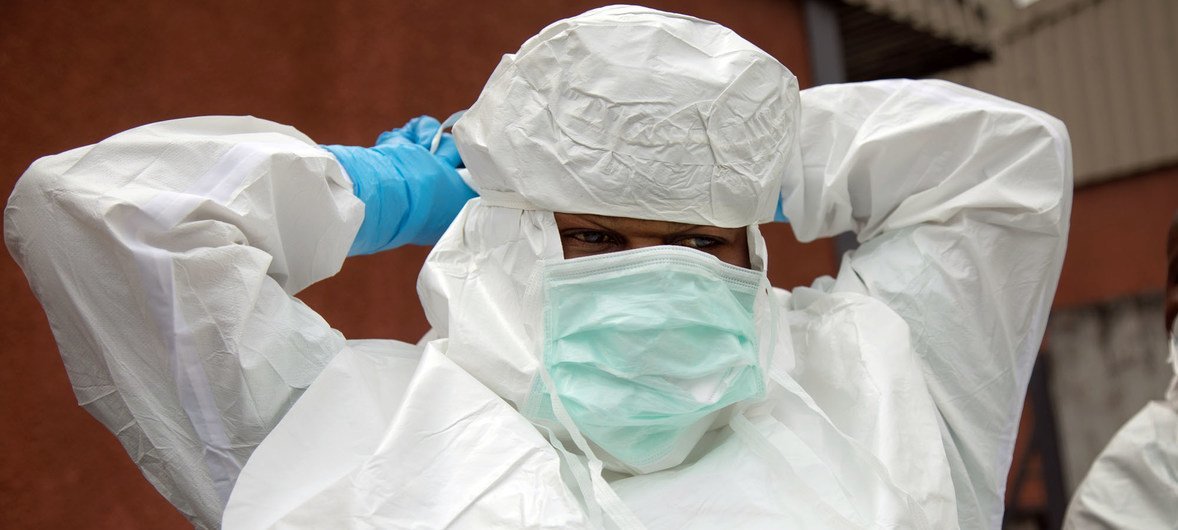 Uma profissional de saúde em Gomas, na República Democrática do Congo, ajusta um traje de proteção branco e uma touca enquanto usa luvas azuis e máscara facial em um necrotério durante o surto de Ebola.