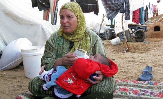Uma mulher deslocada alimenta uma criança em Gaza.