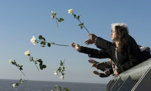 Visitantes lanzan flores blancas al río de la plata como símbolo de respeto en el Parque de la Memoria, Buenos Aires, Argentina.
