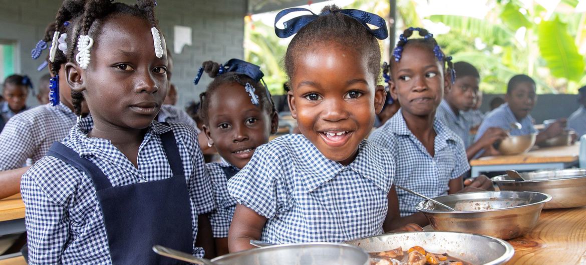 Crianças em idade escolar no Haiti comem em tigelas de metal em um refeitório.