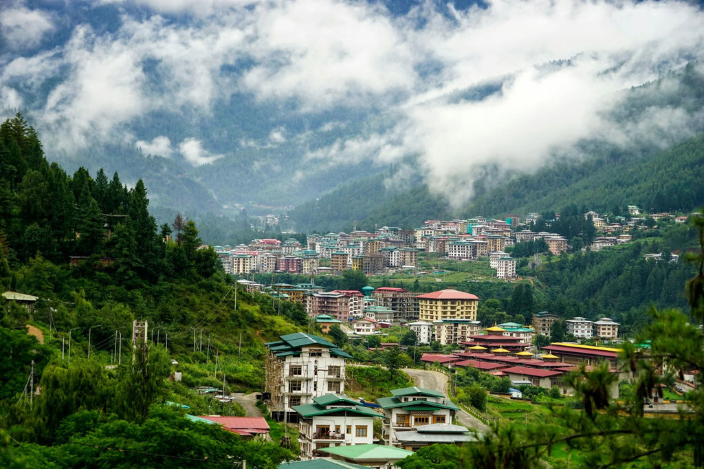 Mandhari ya jiji la Thimphu, Bhutan, lililopo katika bonde lenye milima na mawingu.