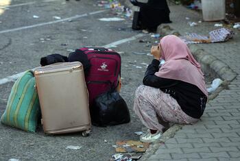 A woman wearing a hijab sits on a curb in Beirut next to her luggage, appearing distressed, amidst debris on the street following a mass evacuation warning.