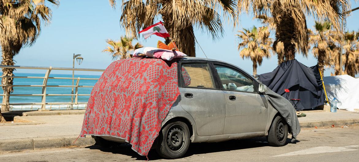 Un refuge provisoire d'une famille déplacée à Beyrouth, au Liban, construit à partir d'une voiture et de couvertures avec un drapeau libanais sur le dessus, près de tentes sur le front de mer.