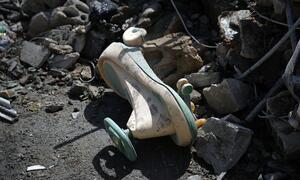 A damaged child's tricycle lies amidst rubble and debris following airstrikes in the Bashura neighborhood of Beirut, Lebanon. The scene depicts the destruction and displacement caused by the conflict.