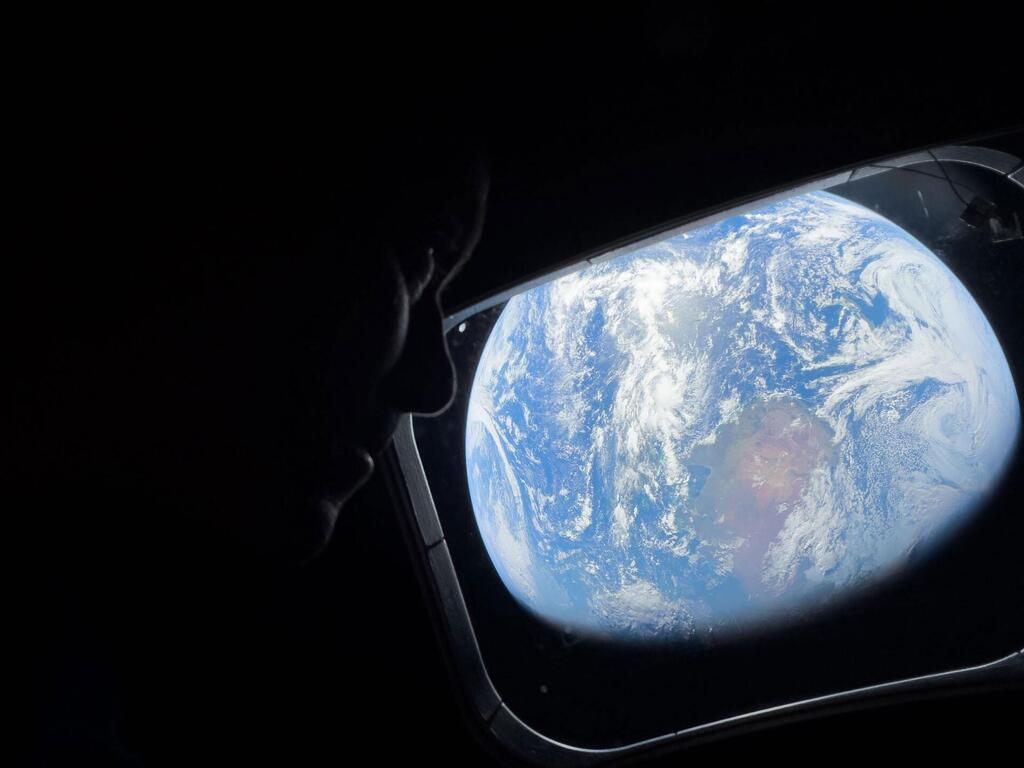 Una silueta de un astronauta mirando la Tierra a través de la ventana de la nave espacial.