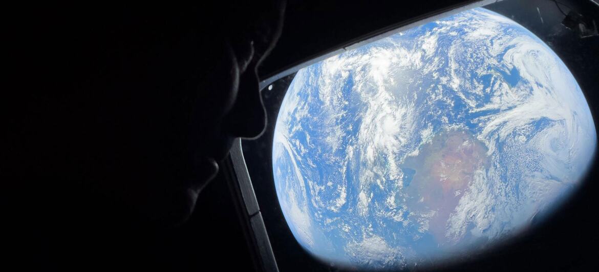 Silhueta de um astronauta olhando para a Terra através da janela da nave espacial.