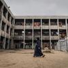 A pregnant woman walks through the courtyard of a damaged school building in Jabalia, Gaza, which serves as a displacement site with UNICEF tents nearby.
