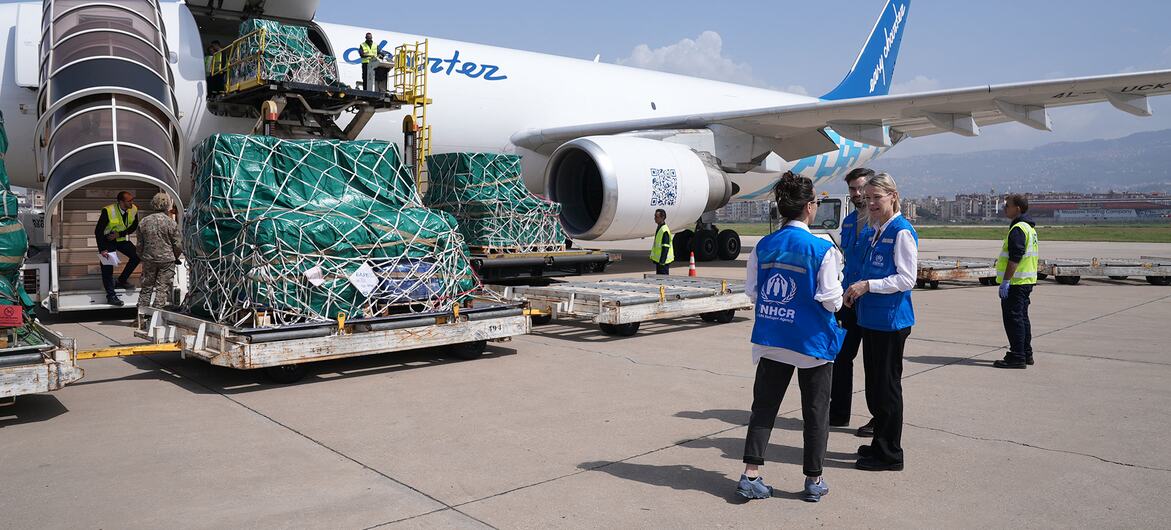 Представитель УВКБ ООН Каролина Линдхольм Биллинг и сотрудники стоят на взлётно-посадочной полосе аэропорта, наблюдая за погрузкой гуманитарных грузов на бортовой самолёт.