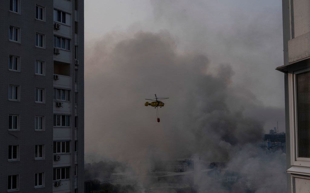 A state emergency service helicopter carries water as it flies over residential Kyiv neighbourhoods blanketed in smoke. 
