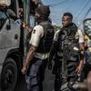 Oficiales de la Policía Nacional de Haití en equipo táctico revisan documentos en un puesto de control en la carretera del aeropuerto cerca de Solino, Puerto Príncipe, en medio de la violencia de pandillas y los desafíos de seguridad.