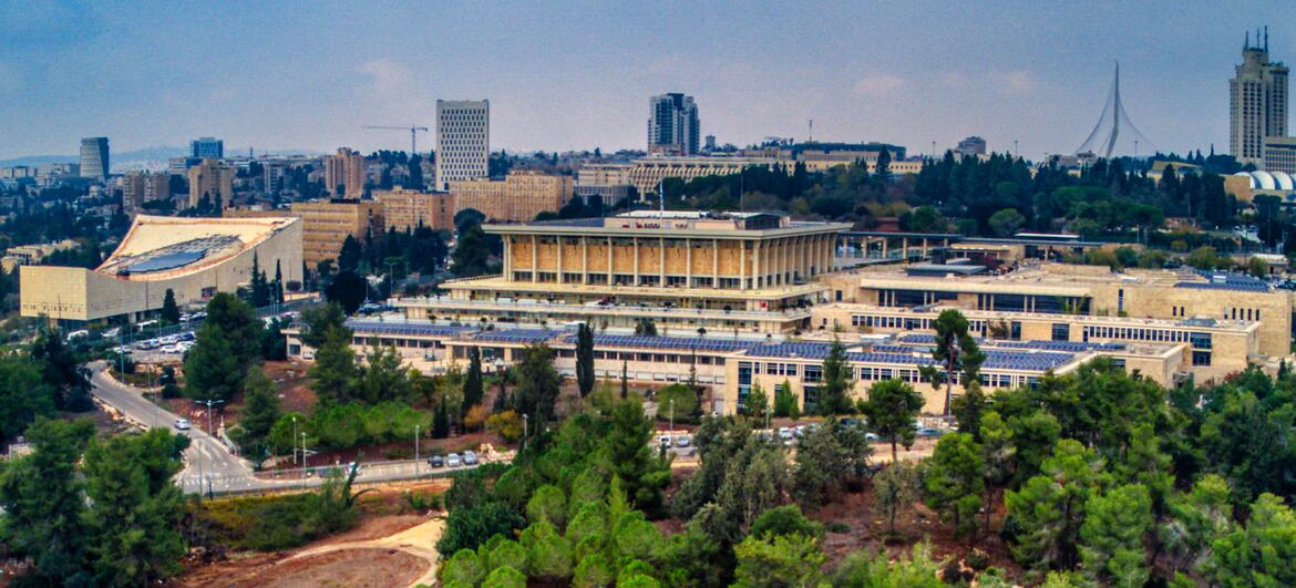 Aerial view of the Knesset building in Jerusalem, Israel, surrounded by greenery and urban skyline.