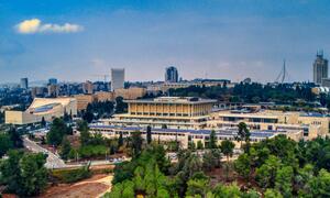 Aerial view of the Knesset building in Jerusalem, Israel, surrounded by greenery and urban skyline.