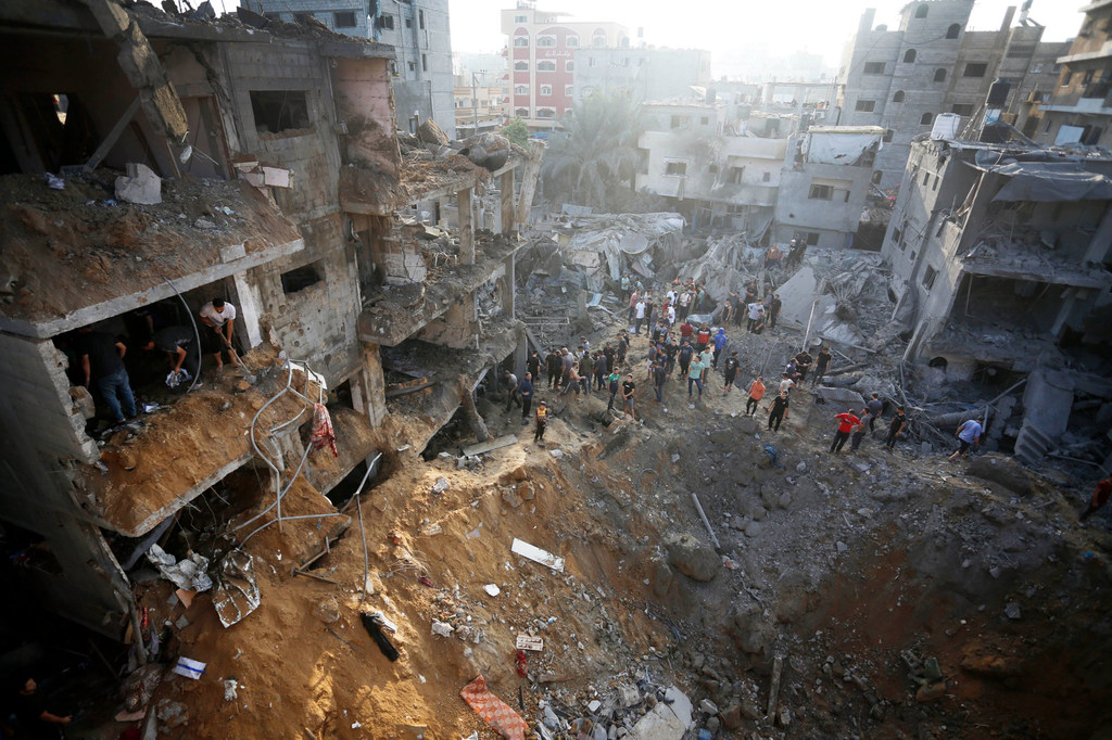 Des gens regardent un cratère de bombe à Maghazi, dans le centre de Gaza.