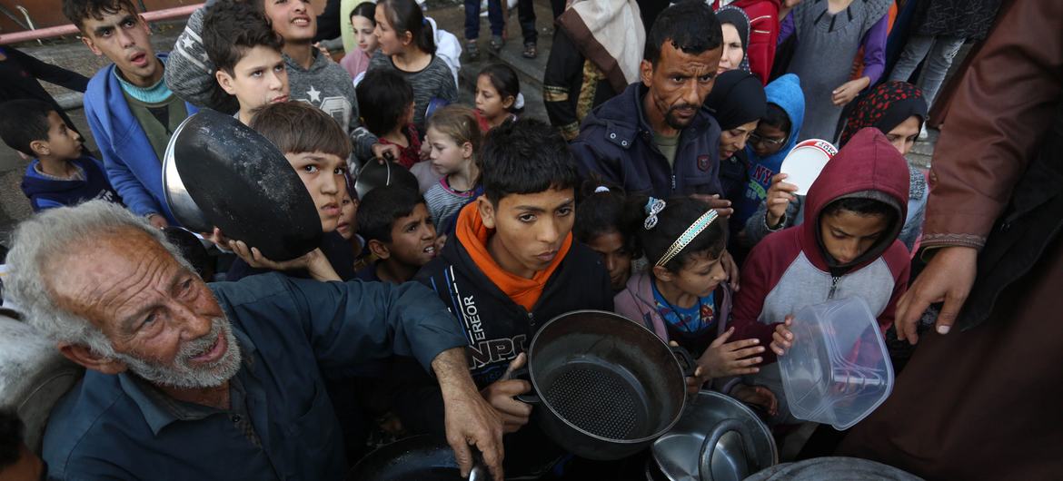 Palestinos desabrigados esperam para coletar alimentos em um ponto de distribuição perto de uma escola que virou abrigo