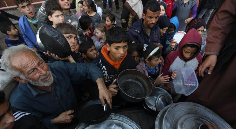 Palestinos deslocados esperam para coletar alimentos em um ponto de distribuição perto de uma escola que virou abrigo em Gaza.