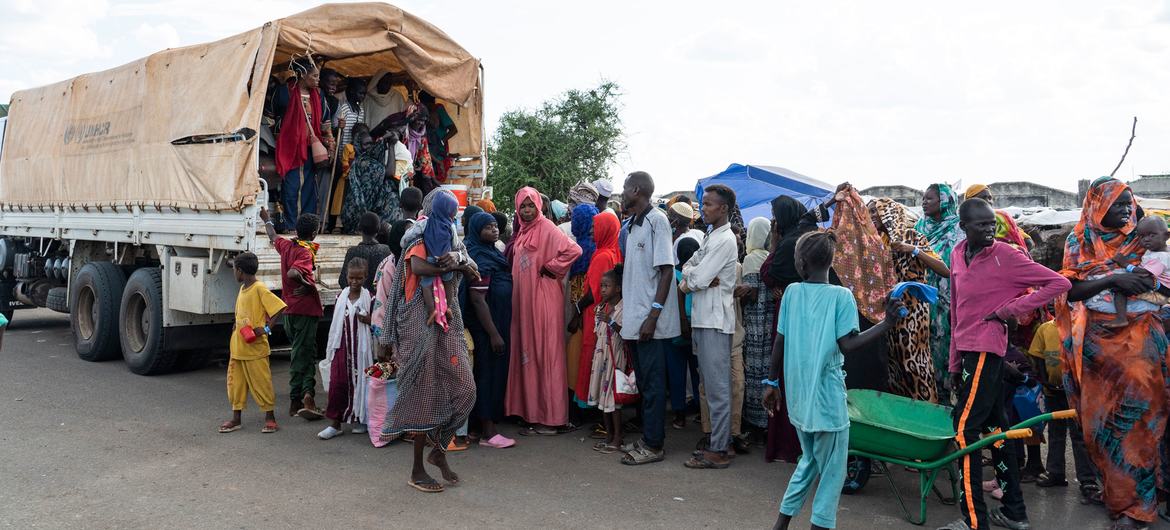 Un grand groupe de réfugiés et de rapatriés, y compris des femmes, des enfants et des hommes, se rassemblent près d'un camion du HCR au centre de transit de Renk, au Soudan du Sud.
