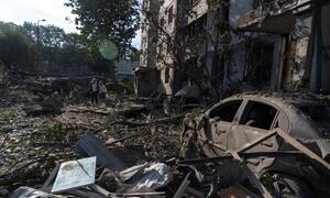 A destroyed car and rubble in a damaged building in Kyiv, Ukraine, with a woman and a child walking through the debris.