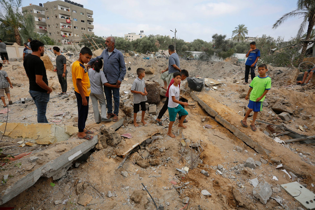 Des hommes et des garçons regardent un cratère de bombe à Gaza.