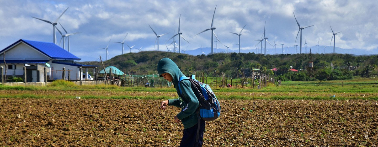 Un écolier passe devant un parc éolien aux Philippines.