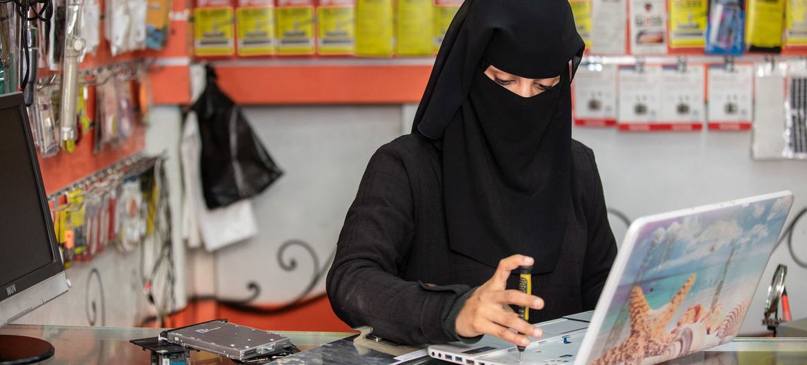 A woman mends a laptop at her phone and computer maintenance shop in Taiz, Yemen.
