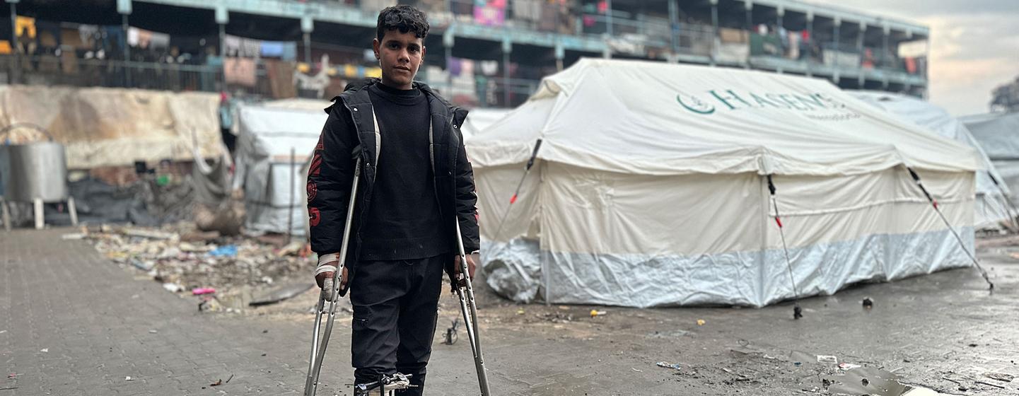 Um menino de muletas está em frente a uma tenda em um campo de deslocados em Gaza.