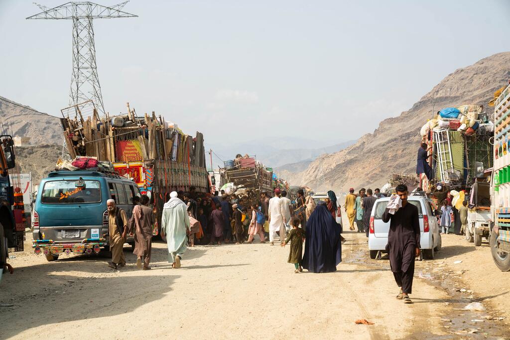 Les familles, y compris les enfants et les personnes âgées, naviguent sur une route bondée et poussiéreuse bordée de véhicules chargés, symbolisant leur voyage de retour en Afghanistan.