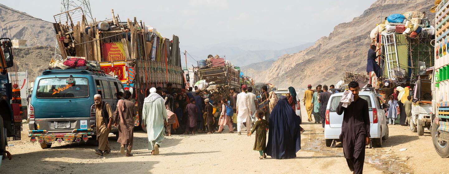 Les familles, y compris les enfants et les personnes âgées, naviguent sur une route bondée et poussiéreuse bordée de véhicules chargés, symbolisant leur voyage de retour en Afghanistan.