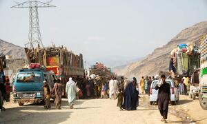 Les familles, y compris les enfants et les personnes âgées, naviguent sur une route bondée et poussiéreuse bordée de véhicules chargés, symbolisant leur voyage de retour en Afghanistan.