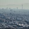 Аэрофотоснимок Тегерана, Иран, демонстрирующий обширную городскую застройку с многочисленными высотными зданиями и выдающейся башней вдали на фоне окутанных дымкой гор.