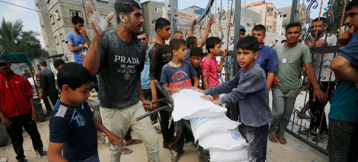 गाजा में संयुक्त राष्ट्र सशस्त्र बलों (UNRWA) द्वारा सहायता वितरण के दौरान पुरुष और लड़के आटे की बोरियां ले जा रहे हैं।