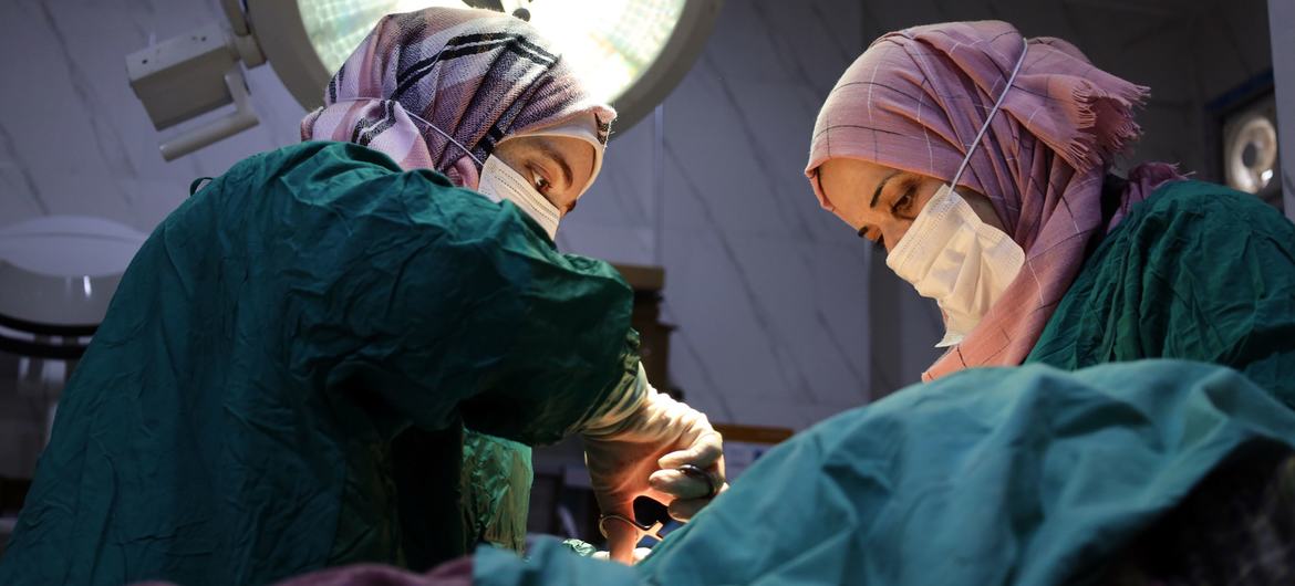 Deux femmes, infirmières en blouses vertes et hijabs, pratiquent une opération sous une puissante lampe chirurgicale dans une maternité en Syrie.