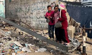 Children in Gaza stand on debris from a destroyed building. 