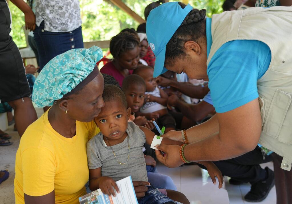 Un trabajador sanitario de UNICEF administra atención médica a un niño mantenido por su madre en una clínica móvil en Boucan Carré, Haití, sirviendo a familias desplazadas afectadas por la violencia.