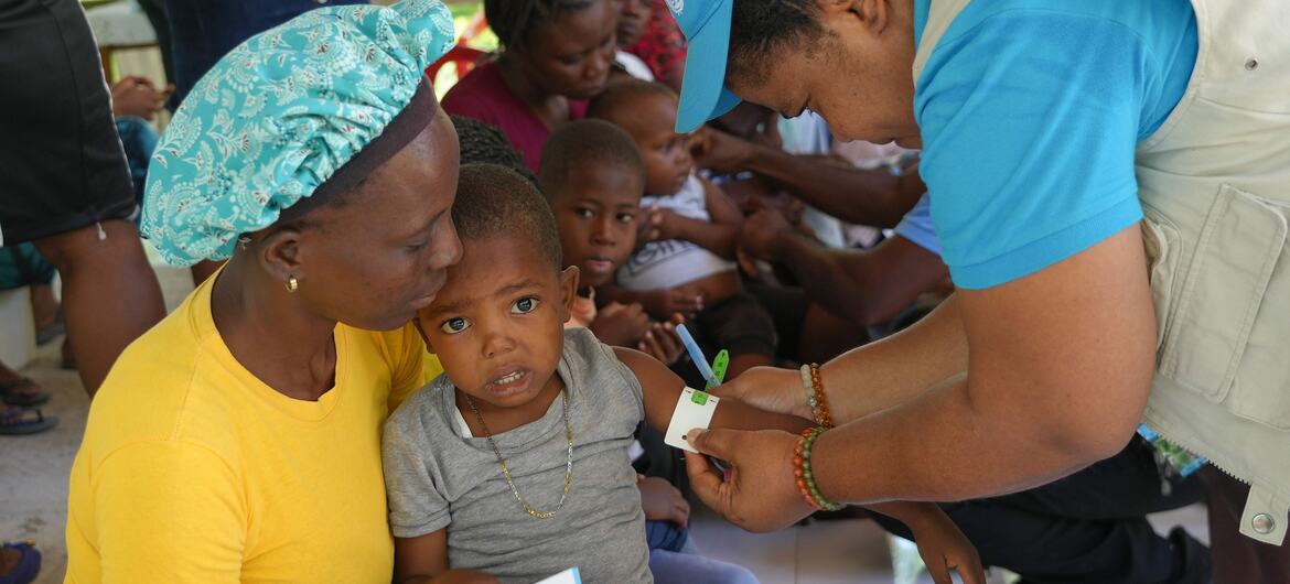 A UNICEF health worker administers medical care to a child held by his mother at a mobile clinic in Boucan Carré, Haiti, serving displaced families affected by violence.