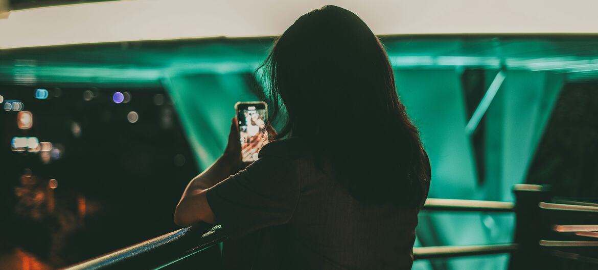 A woman is using her smartphone, possibly engaging with social media content, highlighting issues of cyberbullying and deepfake abuse.