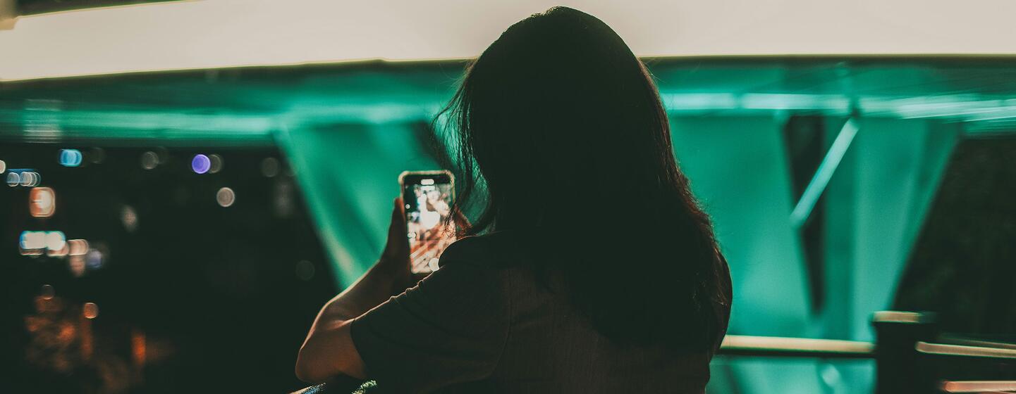 Une femme utilise son smartphone, peut-être pour interagir avec le contenu des médias sociaux, mettant en évidence les problèmes de cyberintimidation et d'abus deepfake.