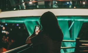 A woman is using her smartphone, possibly engaging with social media content, highlighting issues of cyberbullying and deepfake abuse.