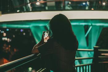 ایک خاتون اپنے اسمارٹ فون کا استعمال کر رہی ہے، ممکنہ طور پر سوشل میڈیا کے مواد سے منسلک ہو رہی ہے، سائبر ہراساں کرنے اور گہری جعلی زیادتی کے مسائل کو اجاگر کر رہی ہے۔