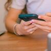 Una persona con piel clara y esmalte de uñas rosa usa un teléfono inteligente, destacando el tema de las redes sociales y la interacción digital.