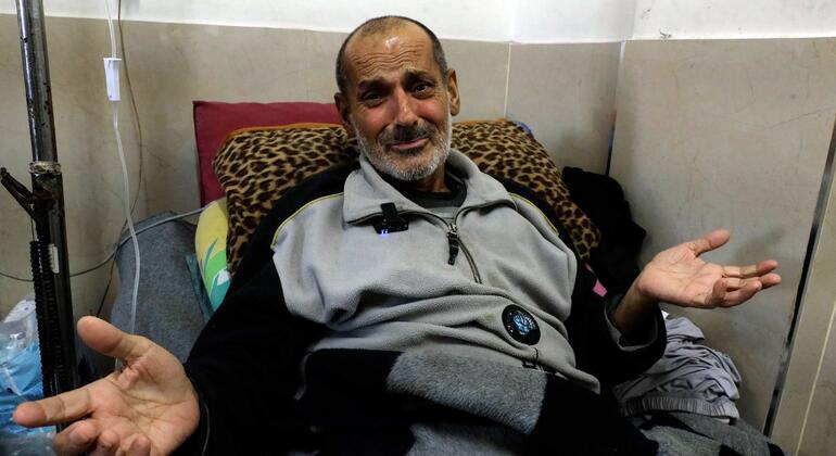 Mundhir Abu Foul, un paciente con cáncer en Gaza, se sienta en una cama de hospital con las manos abiertas, pareciendo hablar o hacer gestos.