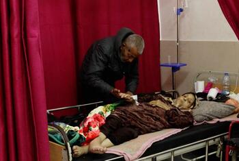 Un patient âgé atteint d'un cancer est allongé dans un lit d'hôpital à Gaza, assisté par un soignant.
