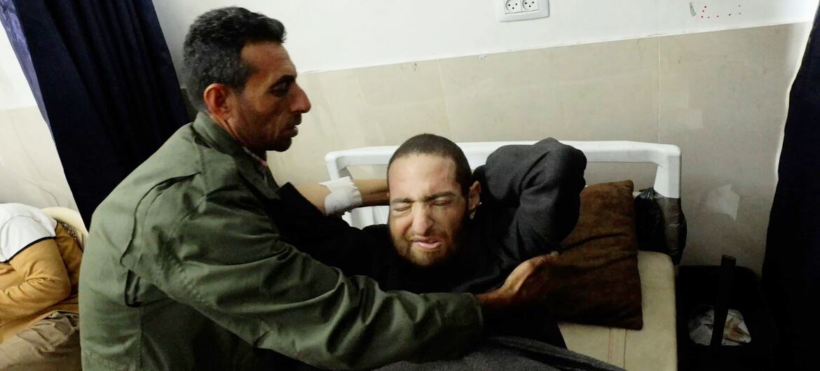 हरे रंग की जैकेट पहने एक आदमी, रायद अबू वारदा, गाजा शहर के अल-शिफा अस्पताल में अपने कैंसर रोगी भाई हामिद अबू वारदा को सांत्वना दे रहा है।