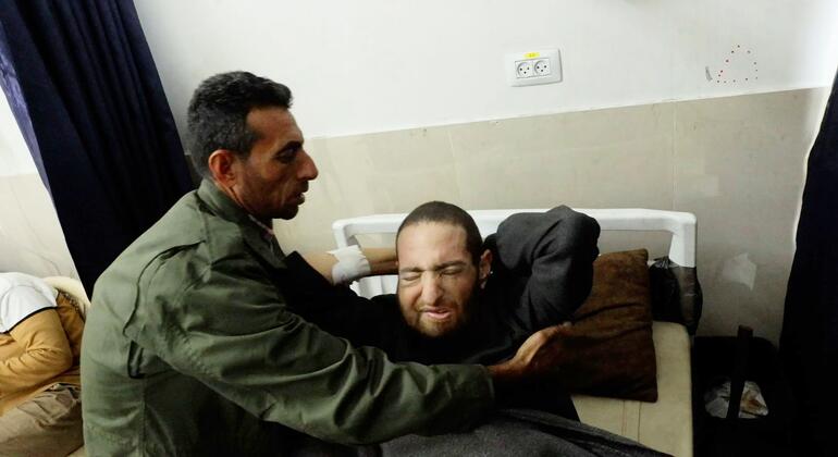 رايد أبو وردة، رجل يرتدي سترة خضراء، يريح شقيقه حميد أبو وردة، مريض السرطان، في مستشفى الشفاء في مدينة غزة.