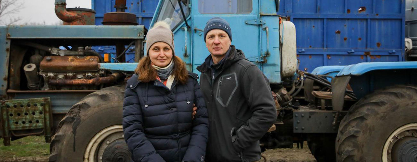 Un homme et une femme ukrainiens se tiennent devant un tracteur bleu, symbolisant les moyens de subsistance agricoles dans une zone minée.