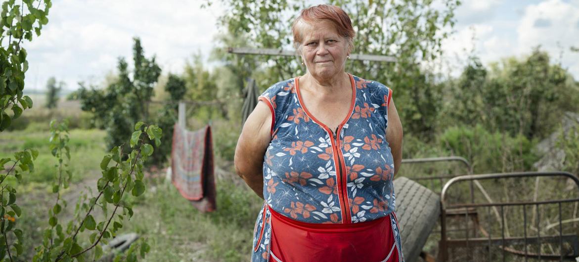 Пожилая украинка стоит в сельской местности, в окружении зелени и бельевой веревки, в то время как Всемирная продовольственная программа и ФАО работают над восстановлением сельскохозяйственного производства.
