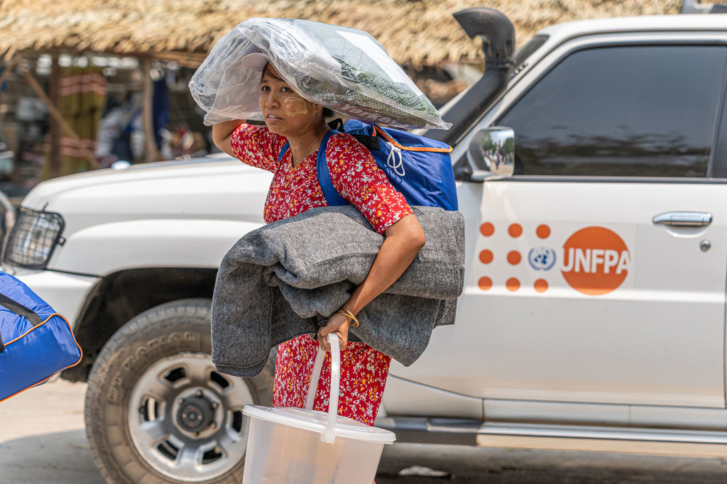 Una mujer lleva suministros de ayuda humanitaria, entre ellos una manta y un cubo, de pie frente a un camión del UNFPA en Myanmar.