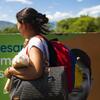 Une femme latino-américaine portant un sac à dos et des sacs se promène à l'extérieur, avec des montagnes en arrière-plan.